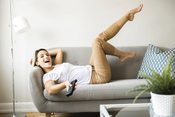 Women watching TV on the sofa at home with remote control — Stock Photo, Image