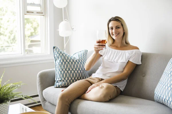 Mujer bebiendo cerveza sentada en un sofá en la sala de estar en casa — Foto de Stock