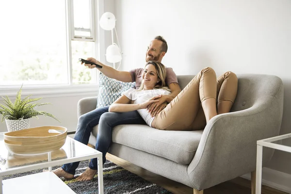 Casal assistindo tv em casa sentado em um sofá confortável na sala de estar em casa — Fotografia de Stock