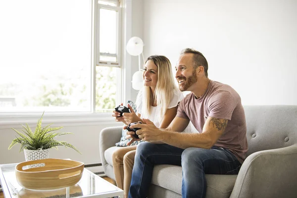 Pareja jugando videojuegos en casa, sentada en un sofá — Foto de Stock