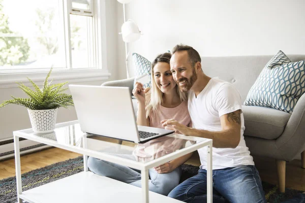 Entusiasmado casal jovem compras on-line, segurando cartão de crédito e olhando para laptop em casa — Fotografia de Stock