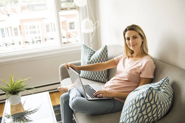 Mujer con un ordenador portátil en el sofá en casa — Foto de Stock