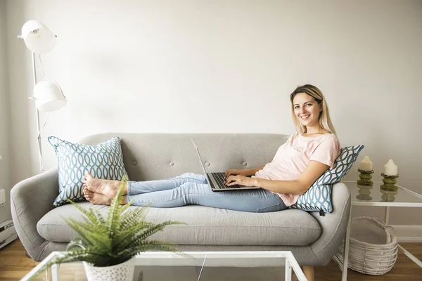 Mujer con un ordenador portátil en el sofá en casa — Foto de Stock