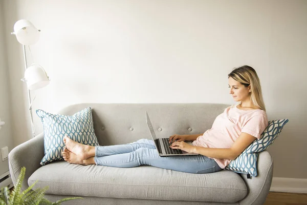Mujer con un ordenador portátil en el sofá en casa — Foto de Stock