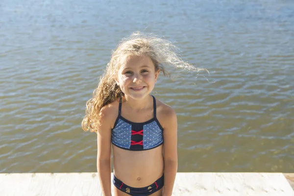Söt liten flicka står leende nära en sjö — Stockfoto