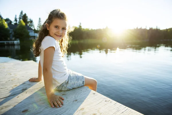 Cute child girl sitting on a wooden platform by the lake. — Stock Photo, Image