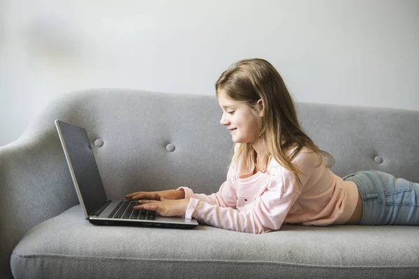 Little girl surfs on the internet lay on the sofa — Stock Photo, Image