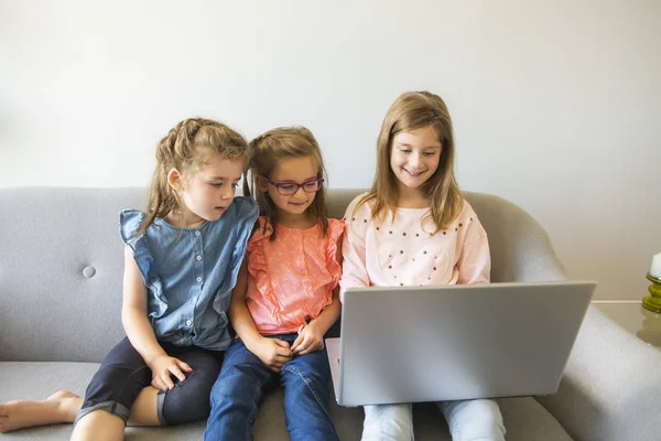 ノート パソコンと自宅のソファに座っている 3 人姉妹の女の子 — ストック写真