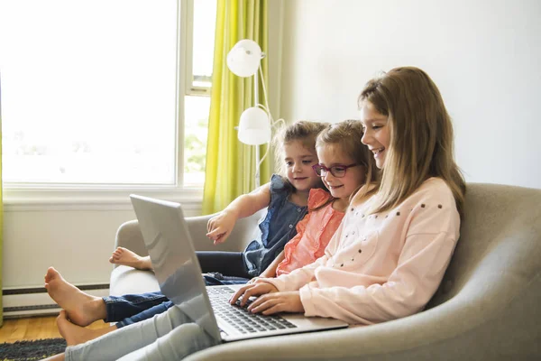 ノート パソコンと自宅のソファに座っている 3 人姉妹の女の子 — ストック写真