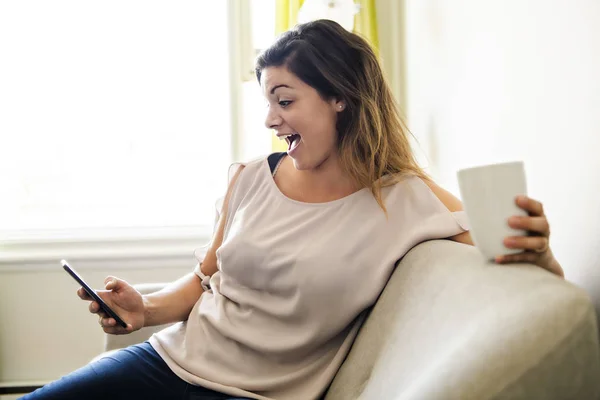 Mujer relajante en sofá conectado con smartphone y tomando café — Foto de Stock