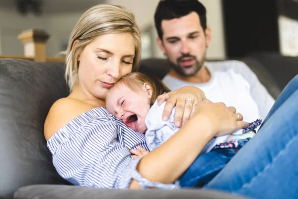 Familia joven con la hija bebé en el sofá en casa, el bebé llorando — Foto de Stock