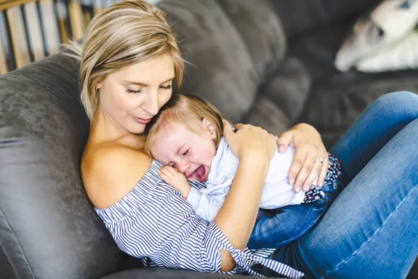 Joven madre con la hija en el sofá en casa, el bebé llorando — Foto de Stock