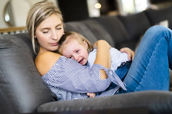 Joven madre con la hija en el sofá en casa, el bebé llorando — Foto de Stock