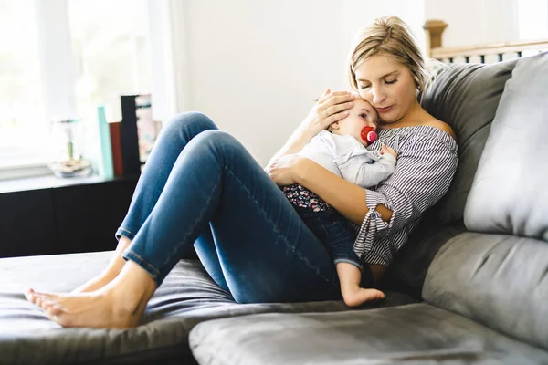 Joven madre con la hija en el sofá en casa, el bebé llorando — Foto de Stock