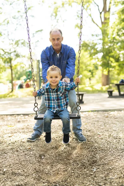 Großvater schubst seinen Enkel auf der Seilschaukel — Stockfoto