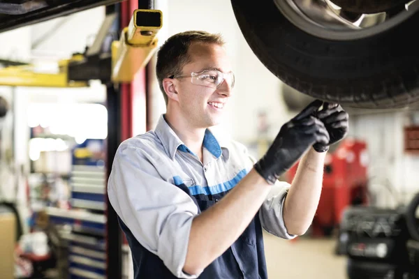 Trabajo mecánico guapo en uniforme trabajando en desgaste de neumáticos de verificación de coche —  Fotos de Stock