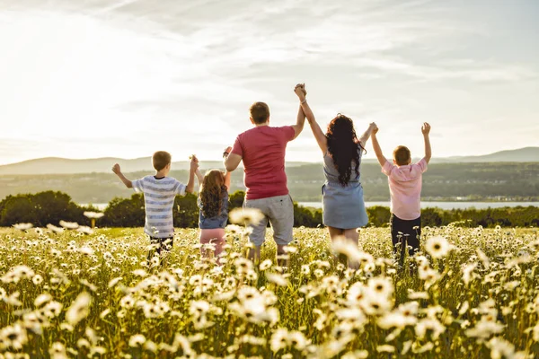 Felice famiglia divertendosi sul campo margherita al tramonto — Foto Stock