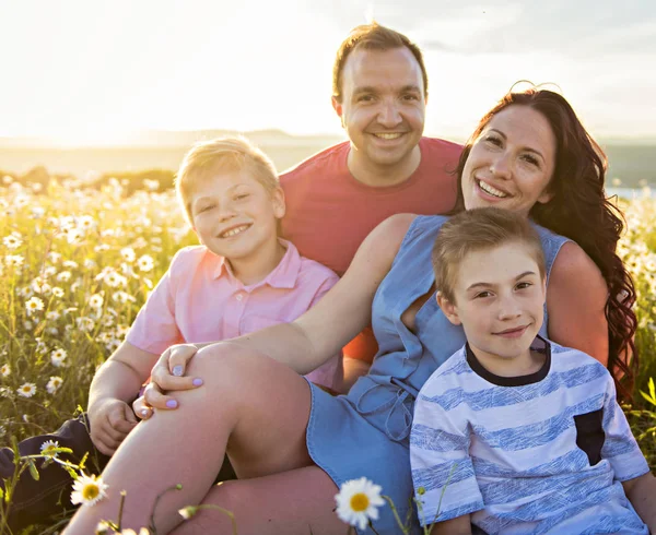 Família feliz se divertindo no campo de margarida ao pôr do sol — Fotografia de Stock