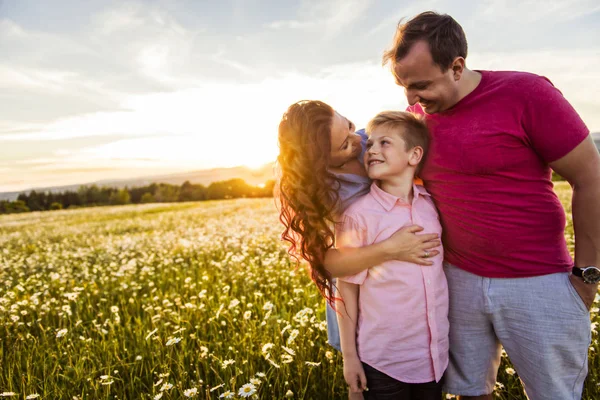 Família feliz se divertindo no campo de margarida ao pôr do sol — Fotografia de Stock