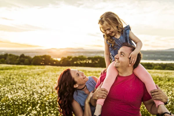 Família ao ar livre passar o tempo juntos Pai, mãe e filha estão se divertindo durante o pôr do sol . — Fotografia de Stock
