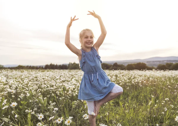 Child on green daisy grass in a summer park sunset time doing balerina — Stock Photo, Image