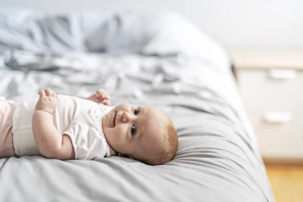 Очаровательная двухмесячная девочка отдыхает в спальне на трикотажном одеяле в солнечное утро — стоковое фото