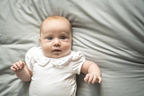 Adorabile bambina di due mesi che si rilassa in camera da letto su una coperta a maglia in una mattina di sole — Foto Stock