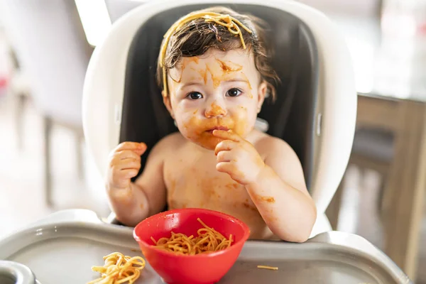 Child girl, eating spaghetti for lunch and making a mess at home in kitchen — Stock Photo, Image