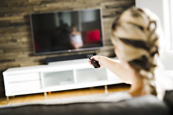 Mujer joven viendo televisión sentada en el sofá de su casa. Vista trasera —  Fotos de Stock