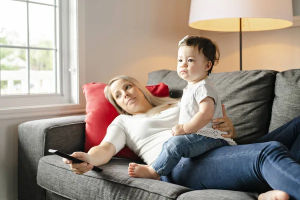 Portrét holčička s matkou v obýváku dívat na televizi — Stock fotografie