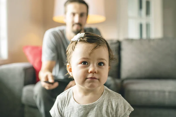 Feliz padre joven en el sofá con control remoto de televisión e hija pequeña — Foto de Stock