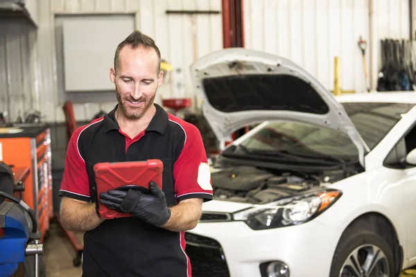 Knappe mechanic gebaseerd op auto in auto reparatiewerkplaats met tablet aan kant — Stockfoto
