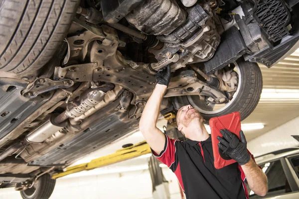 Mecánico guapo basado en el coche en taller de reparación de automóviles con la tableta en la mano — Foto de Stock