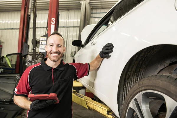 Knappe mechanic gebaseerd op auto in auto reparatiewerkplaats met tablet aan kant — Stockfoto