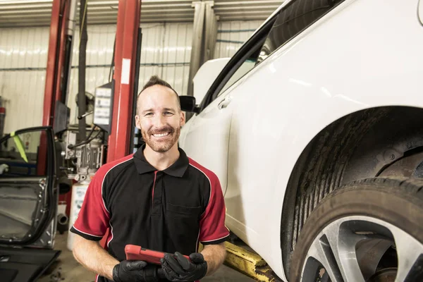 Knappe mechanic gebaseerd op auto in auto reparatiewerkplaats met tablet aan kant — Stockfoto