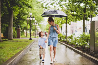 mother and child on a rainy day in a park with umbrella clipart