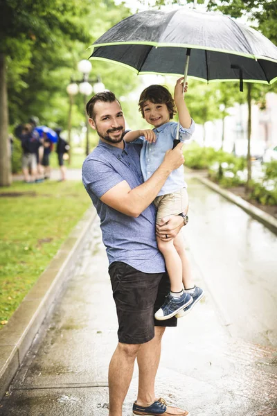 Father and child on a rainy day in a park with umbrella — Stock Photo, Image