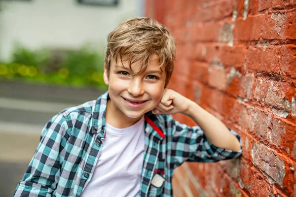 Bedårande söt pojke staing nära en röd tegelvägg — Stockfoto