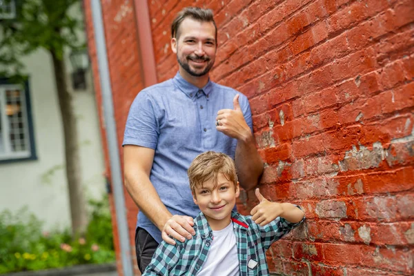 Adorável bonito menino grampeando perto de uma parede de tijolo vermelho com seu pai — Fotografia de Stock