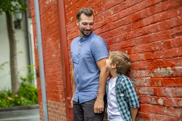 Adorable cute boy staing near a red brick wall with his father — Stock Photo, Image