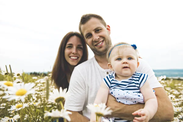 Littlegirl en zijn vader en moeder buitenshuis genieten van op gebied van madeliefjebloemen — Stockfoto