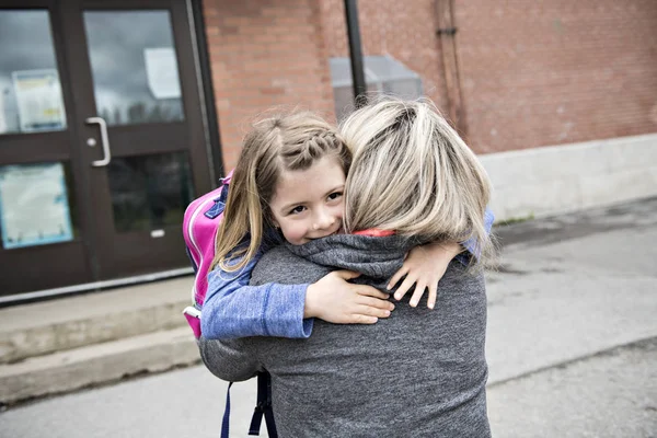 Дівчинка і його мати обіймаються надворі в школі — стокове фото