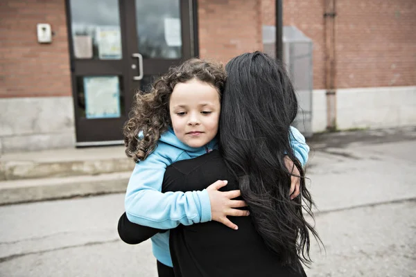 Una niña y su madre abrazándose afuera en la escuela — Foto de Stock