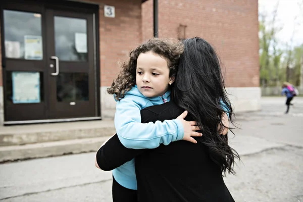 Una bambina e sua madre che si abbracciano fuori a scuola — Foto Stock