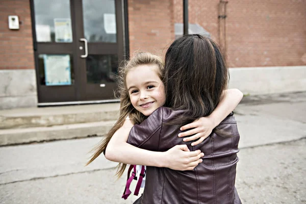 Una bambina e sua madre che si abbracciano fuori a scuola — Foto Stock