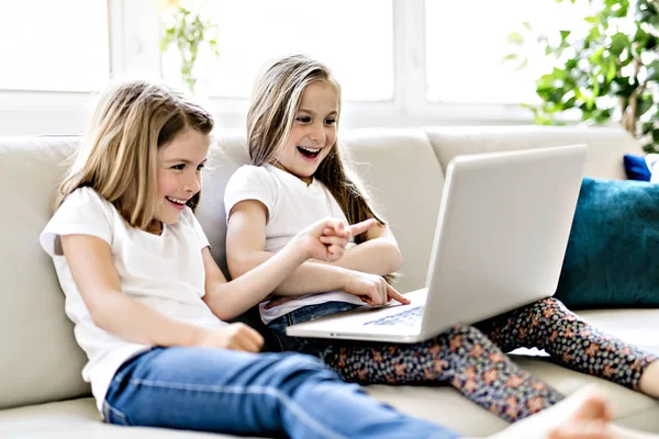 Meninas felizes em casa trabalhando com um laptop no sofá — Fotografia de Stock