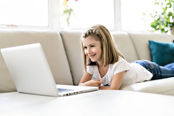 Happy little girl at home working with a laptop on sofa — Stock Photo, Image