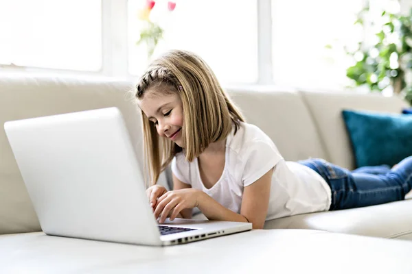 Niña feliz en casa trabajando con un portátil en el sofá —  Fotos de Stock