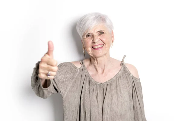 Bejaarde vrouw op studio witte achtergrond met duim omhoog — Stockfoto