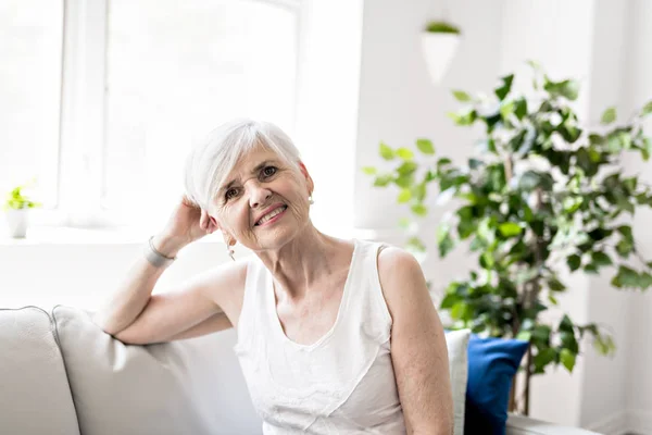 Porträtt av en glad senior kvinna sitter i soffan i vardagsrummet — Stockfoto